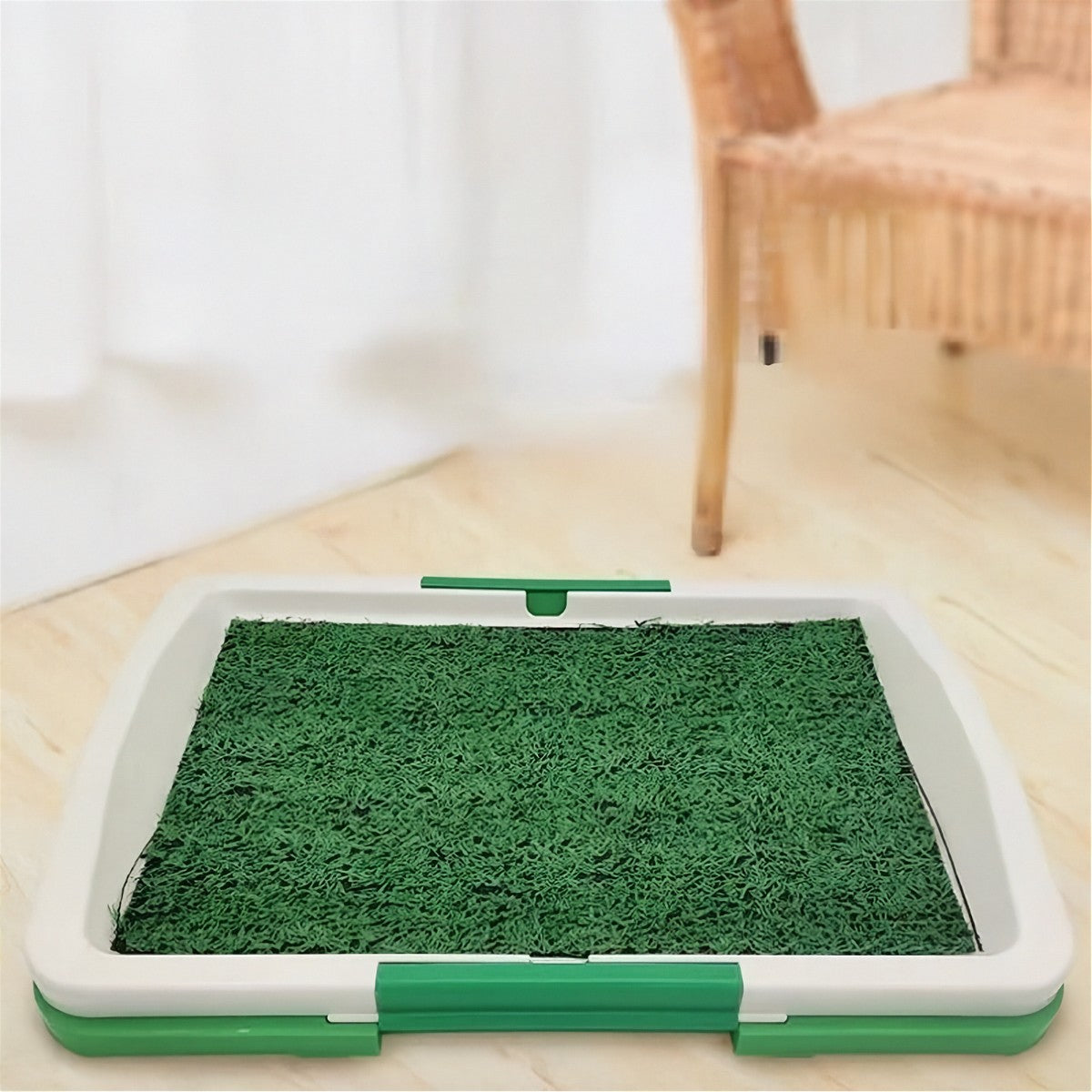 Grass pet toilet tray placed on a wood floor in a living room setting near a wicker chair